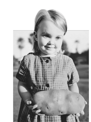 an old black and white photo of little girl holding a giant potato and smiling